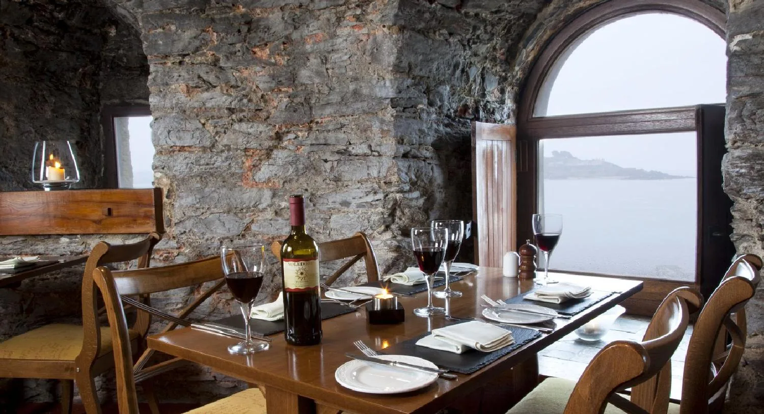 The dining room, with a laid table beside an arched stone gun-port window looking out over the water