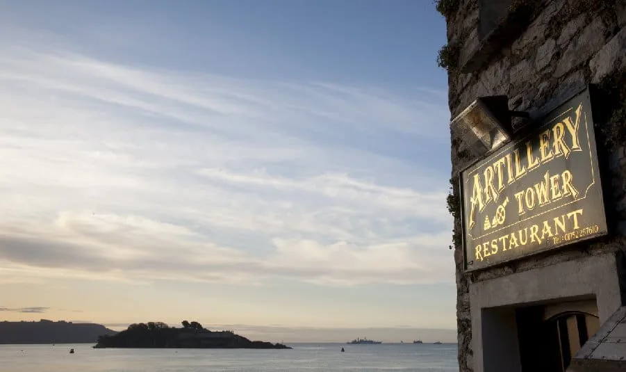 The painted Artillery Tower Restaurant sign on the stone wall at dusk, the Sound and Drake&rsquo;s Island behind