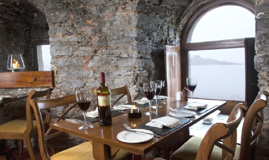 A window table laid with wine glasses, the water of Plymouth Sound filling the arched opening behind it